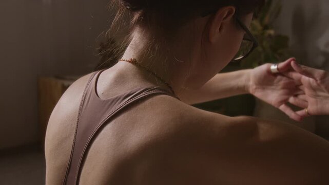 Rear medium close-up of muscular bare upper back and shoulders of unrecognizable young athletic girl performing arm and torso stretches, while preparing for intensive yoga practice at home