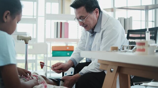 Professional Asian orthopedic doctor examines Black girl's knee bone fracture using a reflex hammer, checks nerve reaction in a child's healthcare, and physical consultation in pediatric hospital.
