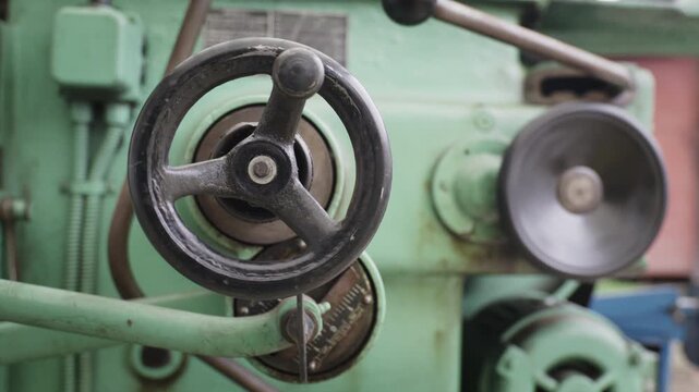 Close-up of a metal shaper machine with mechanical hand wheels in a industrial workshop.