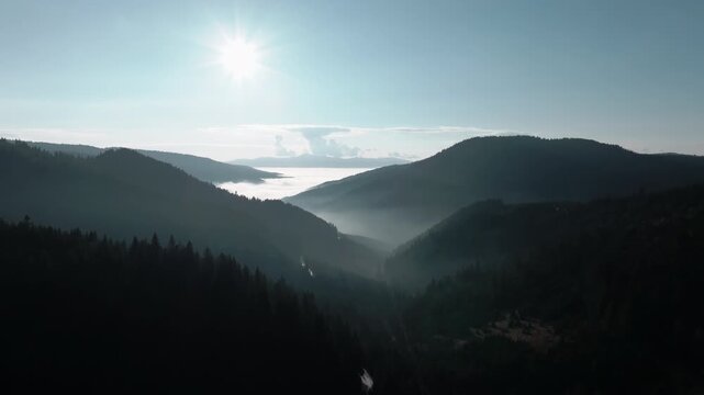 Aerial shot of rolling hills and deep valleys filled with low-hanging fog under a bright, clear sun, of the Cheile Bicazului
