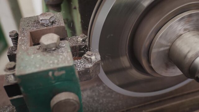 Close-up of a green metal shaper carving a steel block, creating smoke and metallic curls in a workshop.