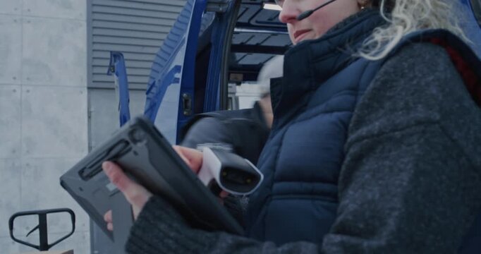 In Cold Snowy Weather, Delivery Crew Loads Parcels Into Van. Female Worker in Headset Manages Scanning and Digital Inventory on Tablet as Male Colleague Lifts and Arranges Boxes. Logistics Operations.