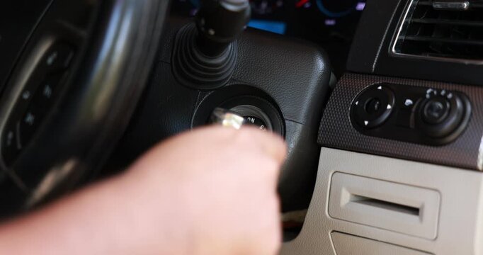 Close up of a man's hand inserting and turning the key in the ignition to start the car engine. Inside view of the vehicle dashboard and steering wheel before driving. High quality 4K video footage.