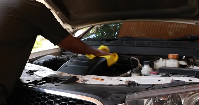 Side view of a male mechanic or driver hands wiping and cleaning the car engine compartment with a yellow microfiber cloth. Auto detailing and vehicle maintenance routine. High quality 4K video.
