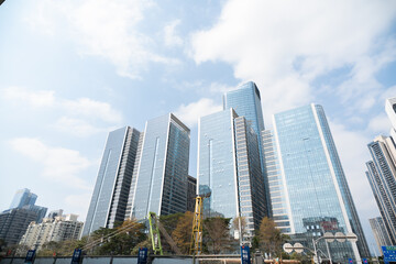 Obraz premium Modern skyscrapers in urban skyline under cloudy blue sky with reflective glass facades and city infrastructure