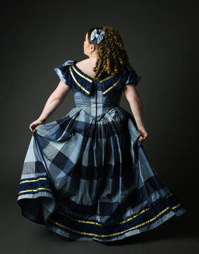 full length portrait of Victorian era Woman in historical classical Blue Ball Gown costume, beautiful plus Size Model. isolated silhouette figure, walking away, back view, on dark studio background.