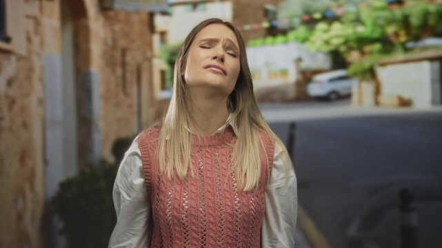 Woman standing on a city street expressing frustration with her hands on her head, showcasing emotions in an outdoor urban setting during daylight.
