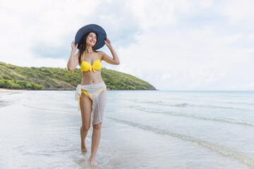 woman is walking on the beach wearing a yellow bikini and a black hat