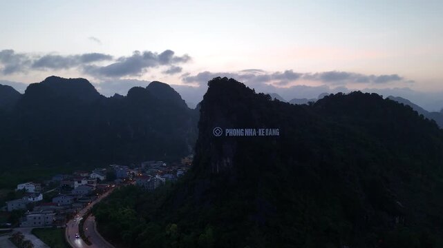 Phong Nha &ndash; Ke Bang National Park, Bo Trach, Quang Binh, Central Vietnam &ndash; 4K aerial drone footage of karst mountains at sunset with illuminated town and iconic Phong Nha sign