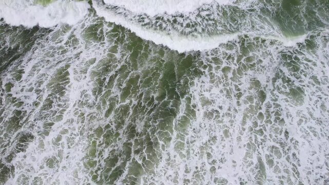 Close establishing aerial backdrop of foamy surf crashing against dark rocks, abstract slow motion
