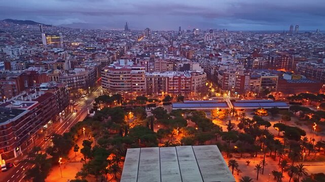 Aerial pan over La Nova Esquerra de l&rsquo;Eixample at night, revealing illuminated streets, dense residential blocks and the vast Barcelona skyline at dusk.