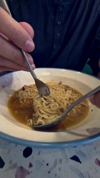Candid scene of twirling gong zai mein or chicken instant noodles in a fork before eating it, iconic staple cafe food in Hong Kong