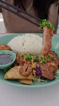 Using chopstick to check the tenderness of a piece of thit nuong or grilled marinated pork paired with rice and goi tom or cabbage salad. Enjoying authentic local traditional Vietnamese food