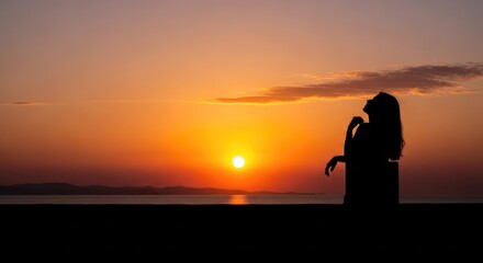 Fototapeta premium A silhouette of a person standing on a beach, gazing at the setting sun over the ocean.