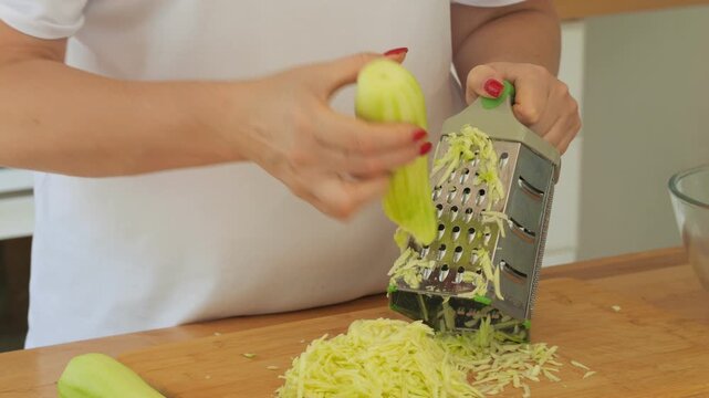Woman is cutting up a green vegetable with a grater. The vegetable is being grated into small pieces