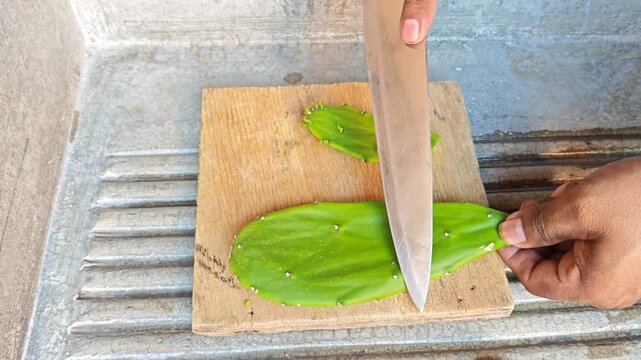 Cleaning prickly pear cactus on wooden board with knife