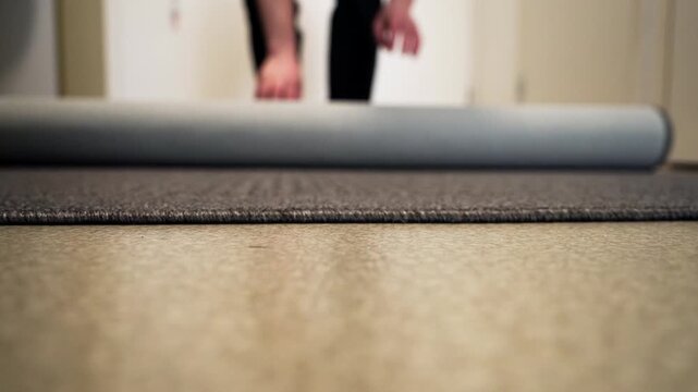 Person unrolls grey carpet on floor