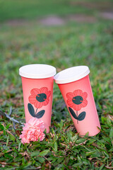 Fototapeta premium Two Pink Floral Paper Cups Standing on Grass