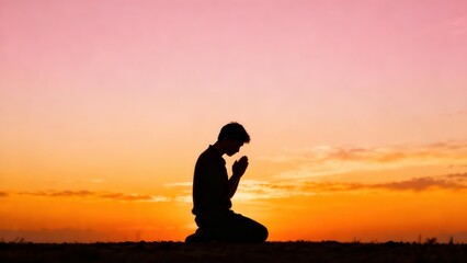 Obraz premium Man kneels in prayer with hands pressed together against a beautiful orange and pink sunset sky at dusk, creating a peaceful silhouette of faith and devotion.