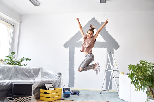 Carefree woman with hand raised jumping against wall at home