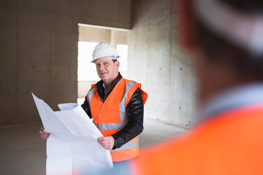 Man with plan wearing safety vest in building under construction
