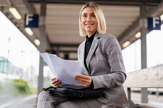 Smiling young businesswoman with papers at the train station