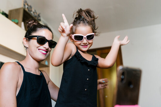 Smiling mother and daughter dancing while recording video on smart phone at home