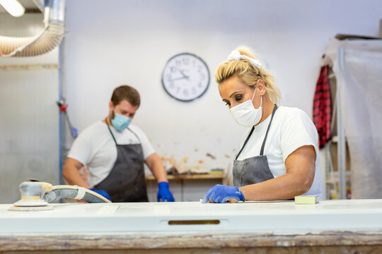 Woman with face mask working by workbench with coworker standing in background at workshop