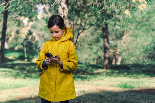 Girl wearing yellow raincoat in nature looking at compass