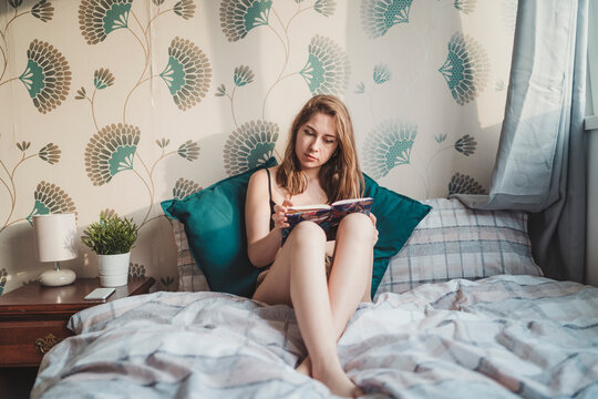 Attractive young woman sitting in bed at home with book