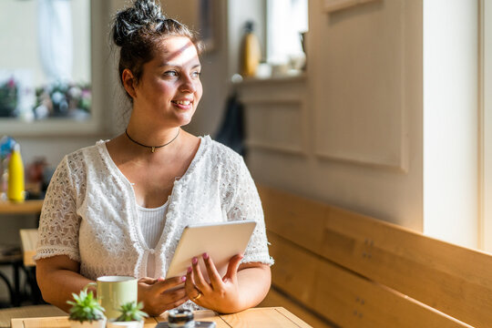 Thoughtful young woman with digital tablet sitting at table in coffee shop