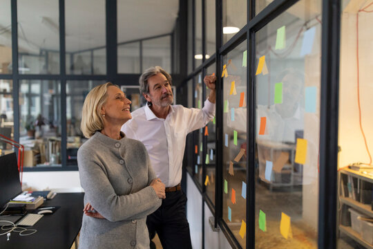 Colleagues looking at sticky notes at glass pane in office