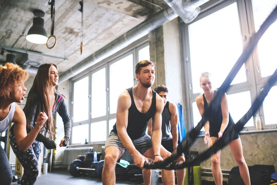 Group of young fit people cheering at man exercising with ropes in gym