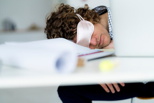 Overworked businessman sleeping at his desk wearing a sleeping mask
