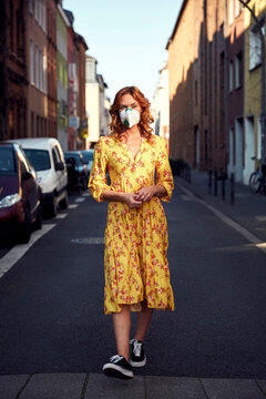 Red-haired woman wearing a FFP2 face mask and walking on empty road