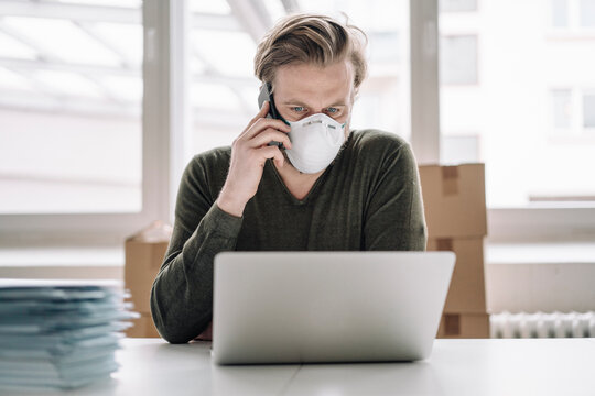 Businessman wearing protective mask and using laptop and cell phone