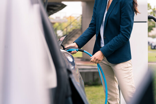 Mature businesswoman charging electric car at Station