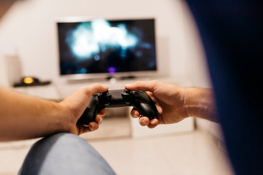 Hands of young male gamer holding controller while playing at home