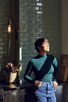 Smiling woman standing in kitchen at home with closed eyes
