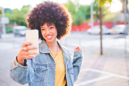 Happy young woman with afro hairdo taking a selfie in the city