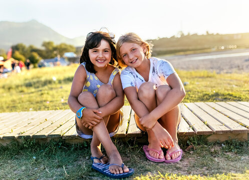 Portrait of two best friends sitting side by side on boardwalk