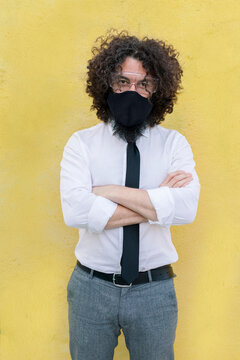 Businessman wearing face mask and eyeglasses standing with arms crossed against wall