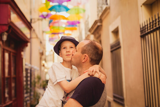 France, Languedoc, Beziers, father kissing son with colorful umbrellas in background