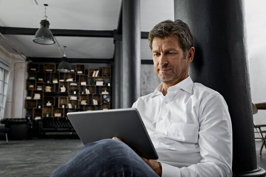 Mature man sitting on the floor using digital tablet in loft flat