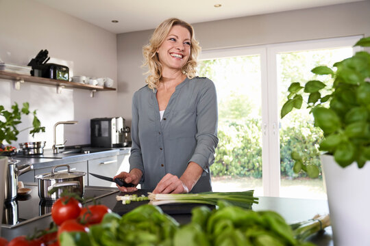 Smiling woman cutting spring onions in kitchen