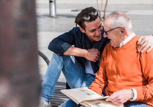 Happy senior man and adult grandson with photo album outdoors