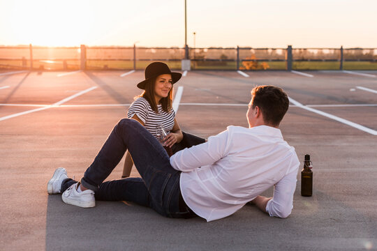 Young couple sitting on parking level at sunset with beer bottles