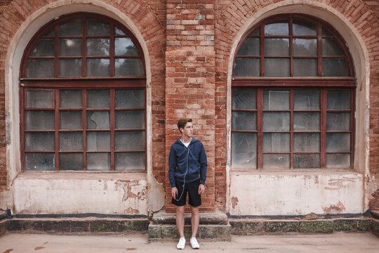Young man with earphones at brick building looking around