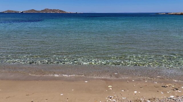 Paros Island,slow motion of the crystal clear waves washing the sandy beach on a sunny day. Shades of blue from light to dark on sea.
