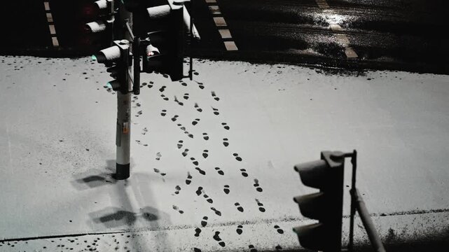 Fresh footsteps in the snow at night near a road and traffic light